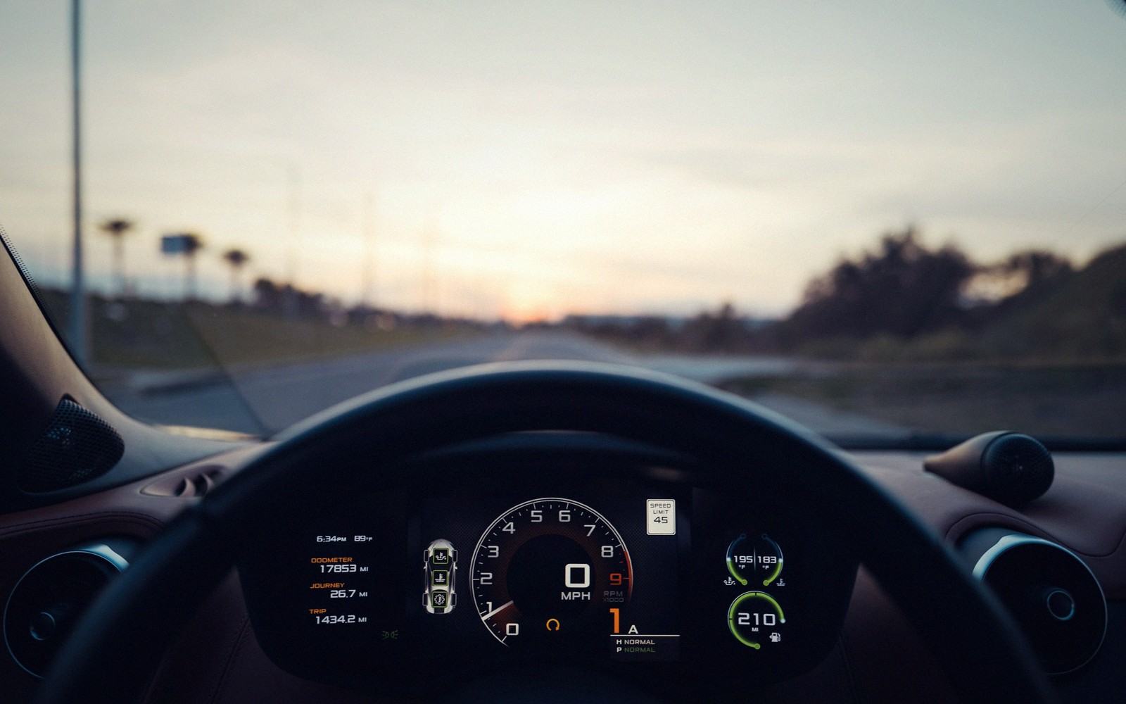 Digital speedometer and dashboard display seen through a car's steering wheel at dusk