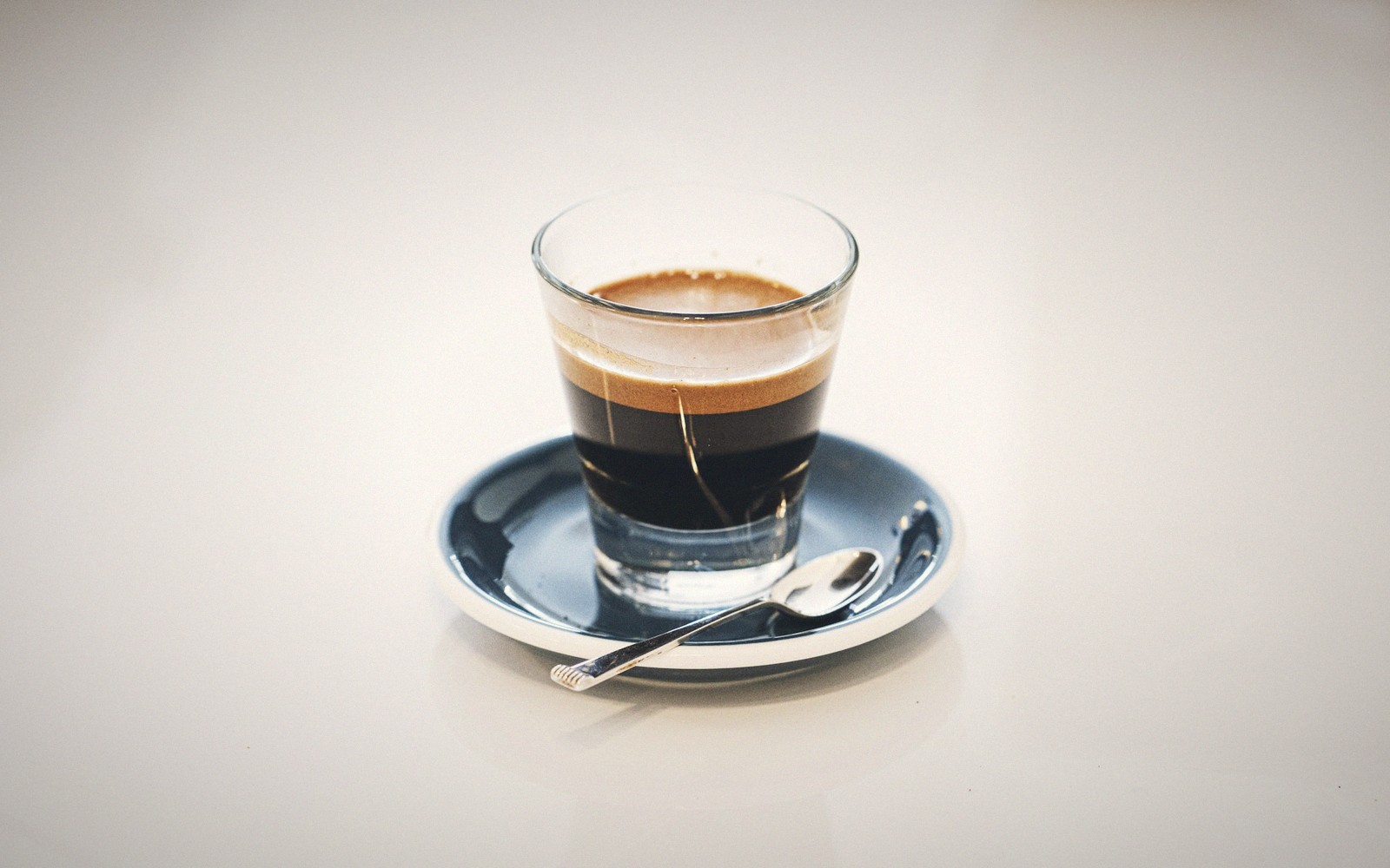 Espresso shot with crema in a small glass on a blue saucer with spoon